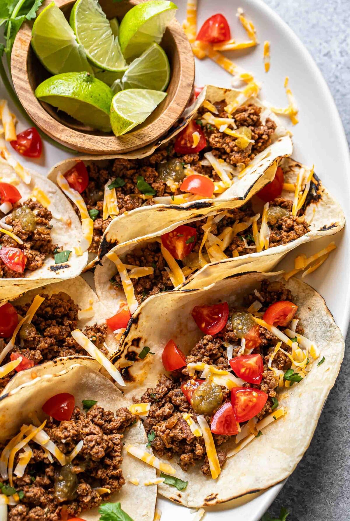 Ground beef tacos on a serving platter with a bowl of lime wedges.