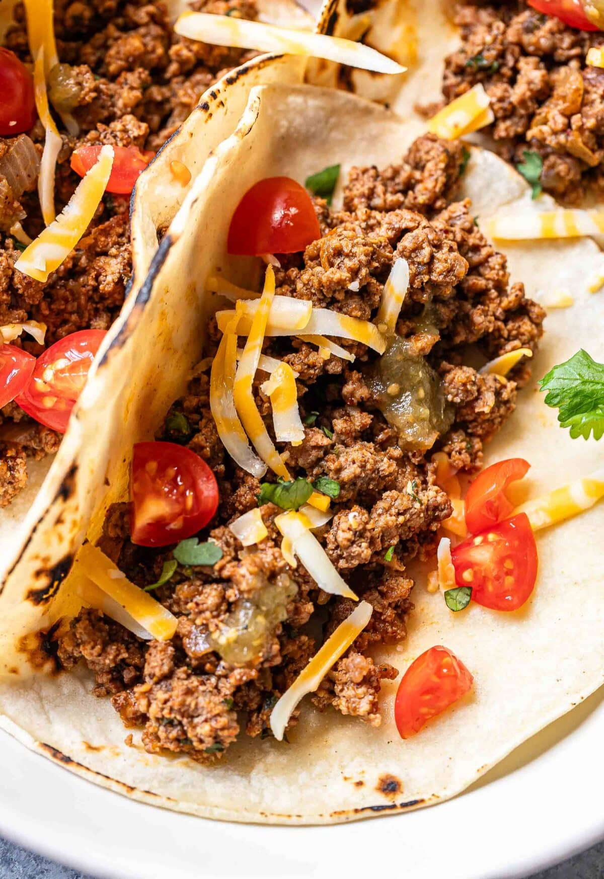 Ground beef taco in a corn tortilla topped with shredded cheese and tomatoes.
