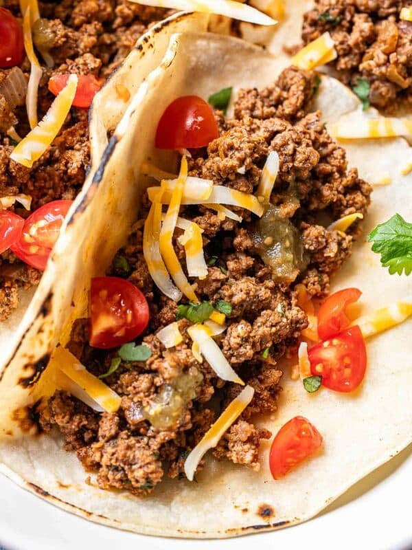 Ground beef taco in a corn tortilla topped with shredded cheese and tomatoes.
