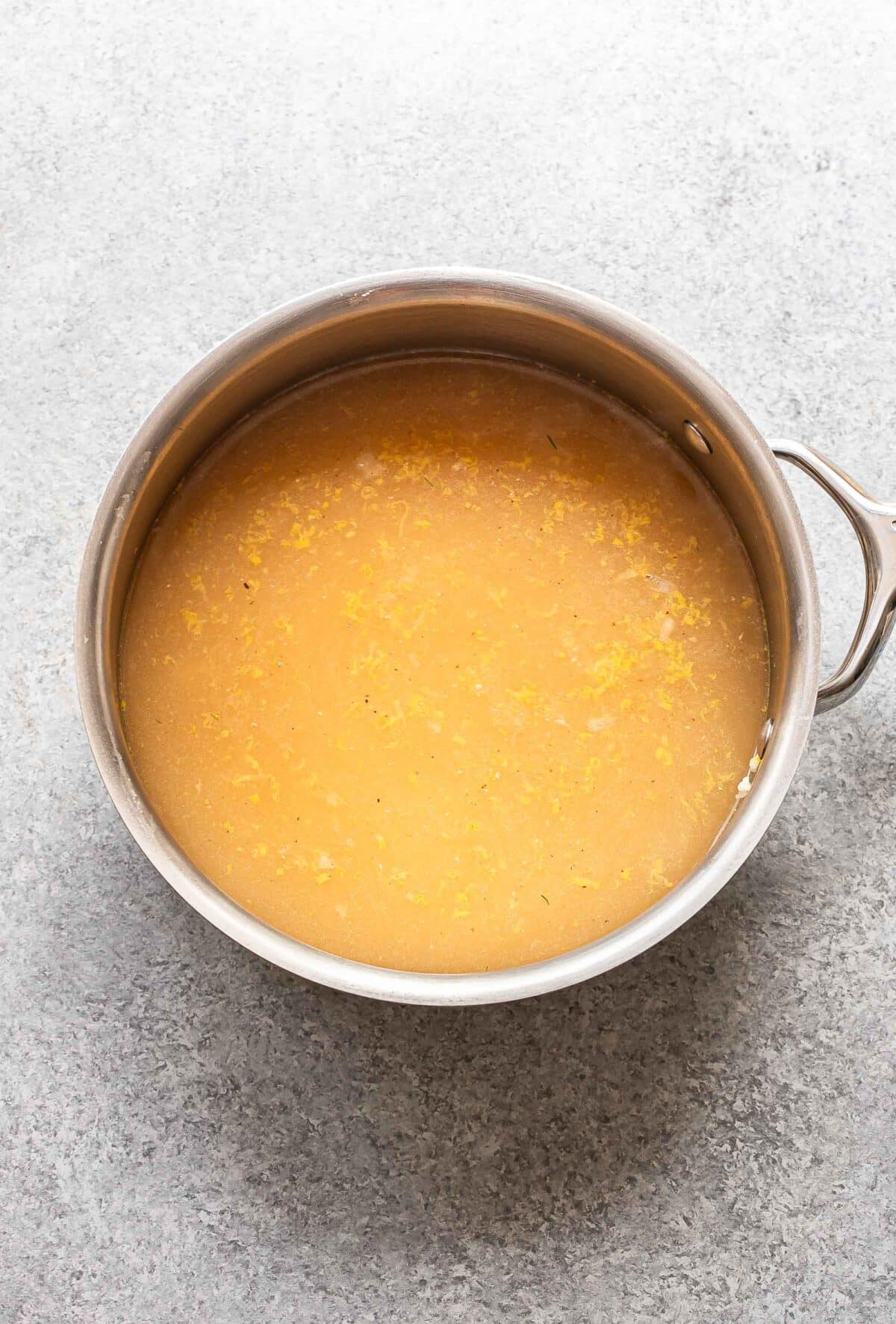 Rice with chicken broth in a saucepan before it's been cooked.