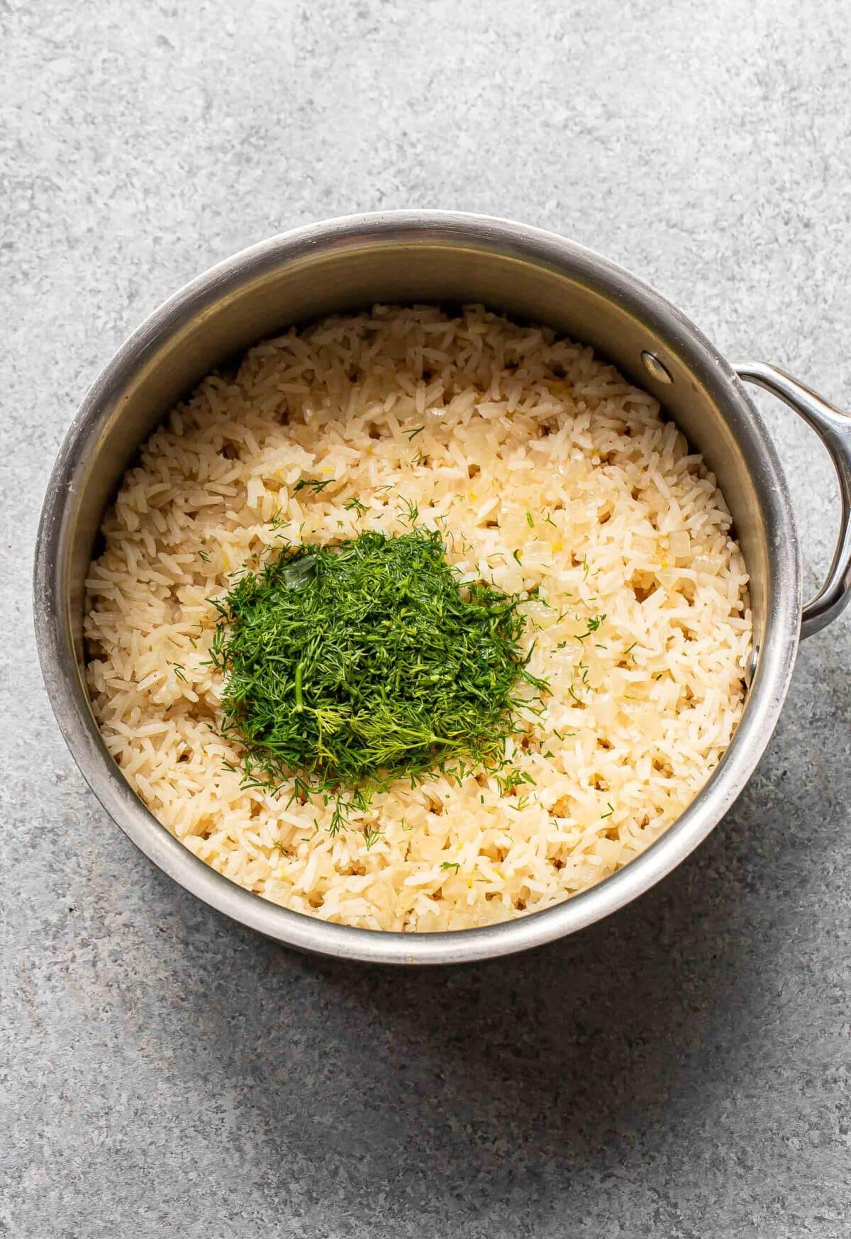 Cooked lemon rice with chopped dill on top of it in a saucepan.