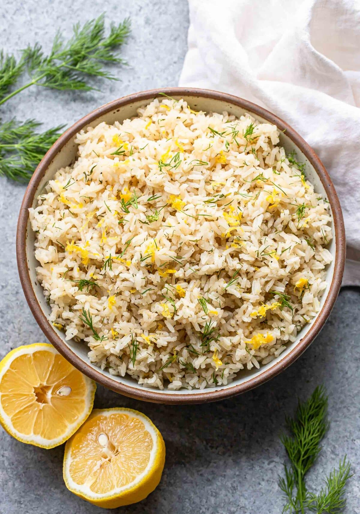 Lemon rice with dill in a serving bowl with a lemon cut in half next to it.