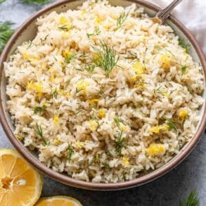 Lemon rice with dill in a serving bowl with a lemon cut in half next to it.