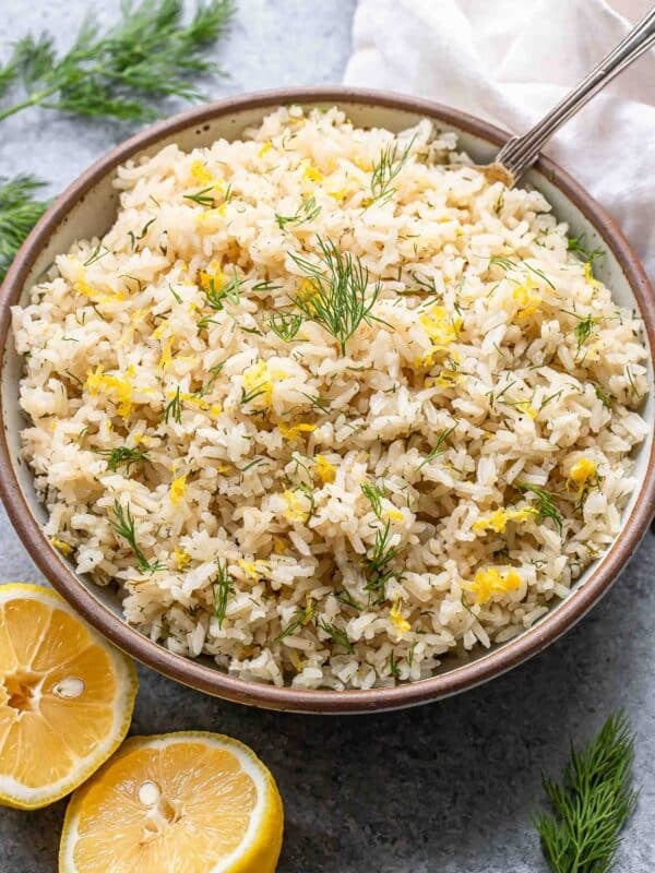 Lemon rice with dill in a serving bowl with a lemon cut in half next to it.