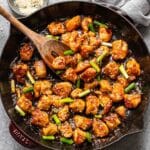 Mongolian chicken in a skillet with a wooden serving spoon.