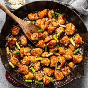 Mongolian chicken in a skillet with a wooden serving spoon.