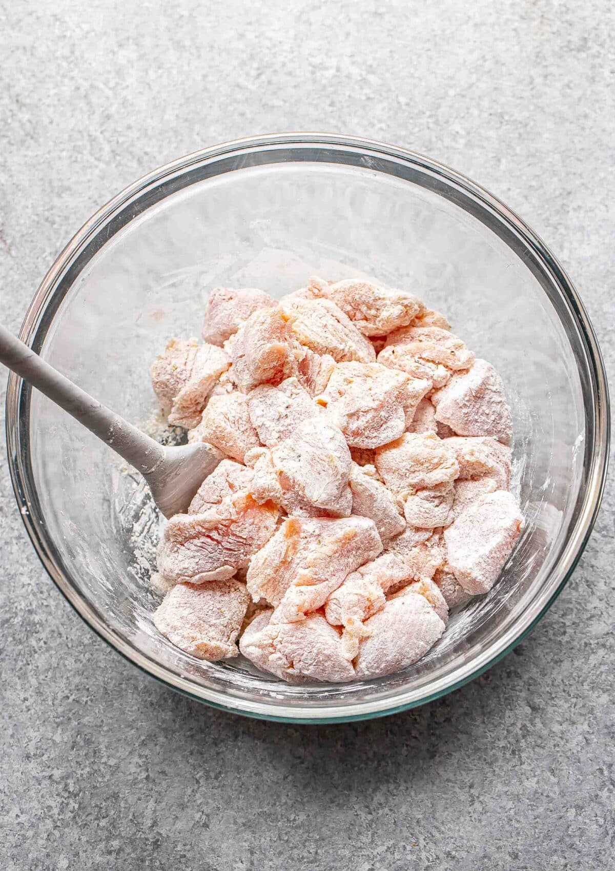 Pieces of chicken coated in cornstarch in a glass bowl.
