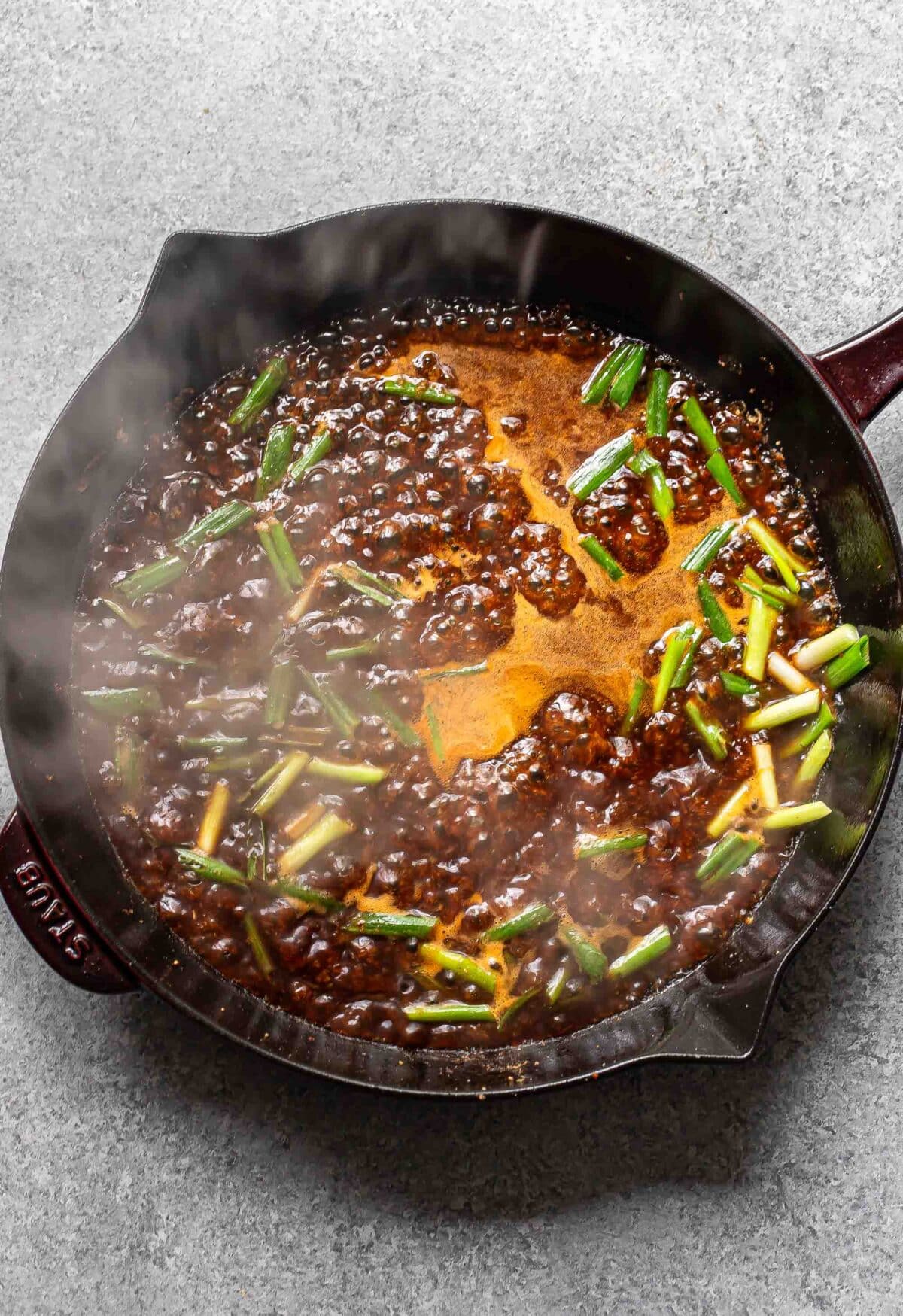 Sliced scallions and the sauce for the mongolian chicken in a skillet.