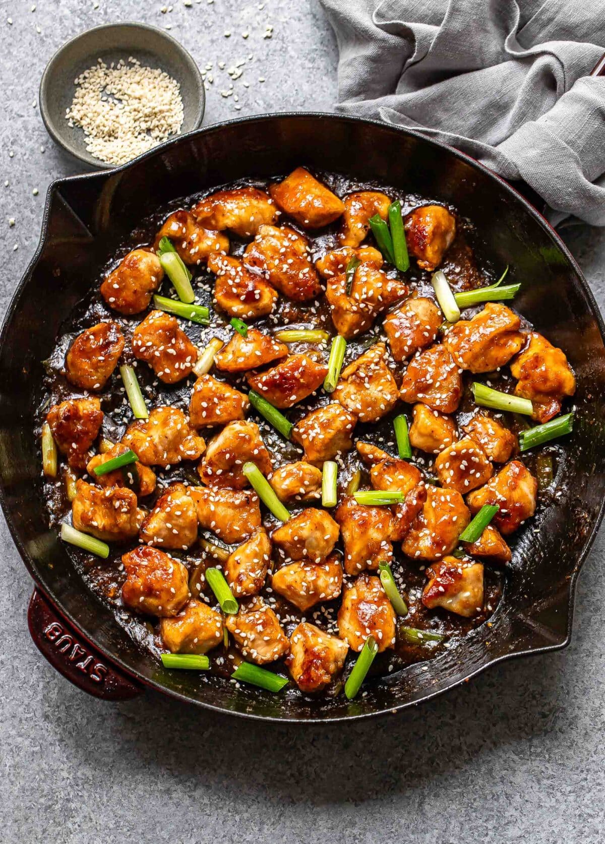 Mongolian chicken in a skillet with scallions and sesame seeds.