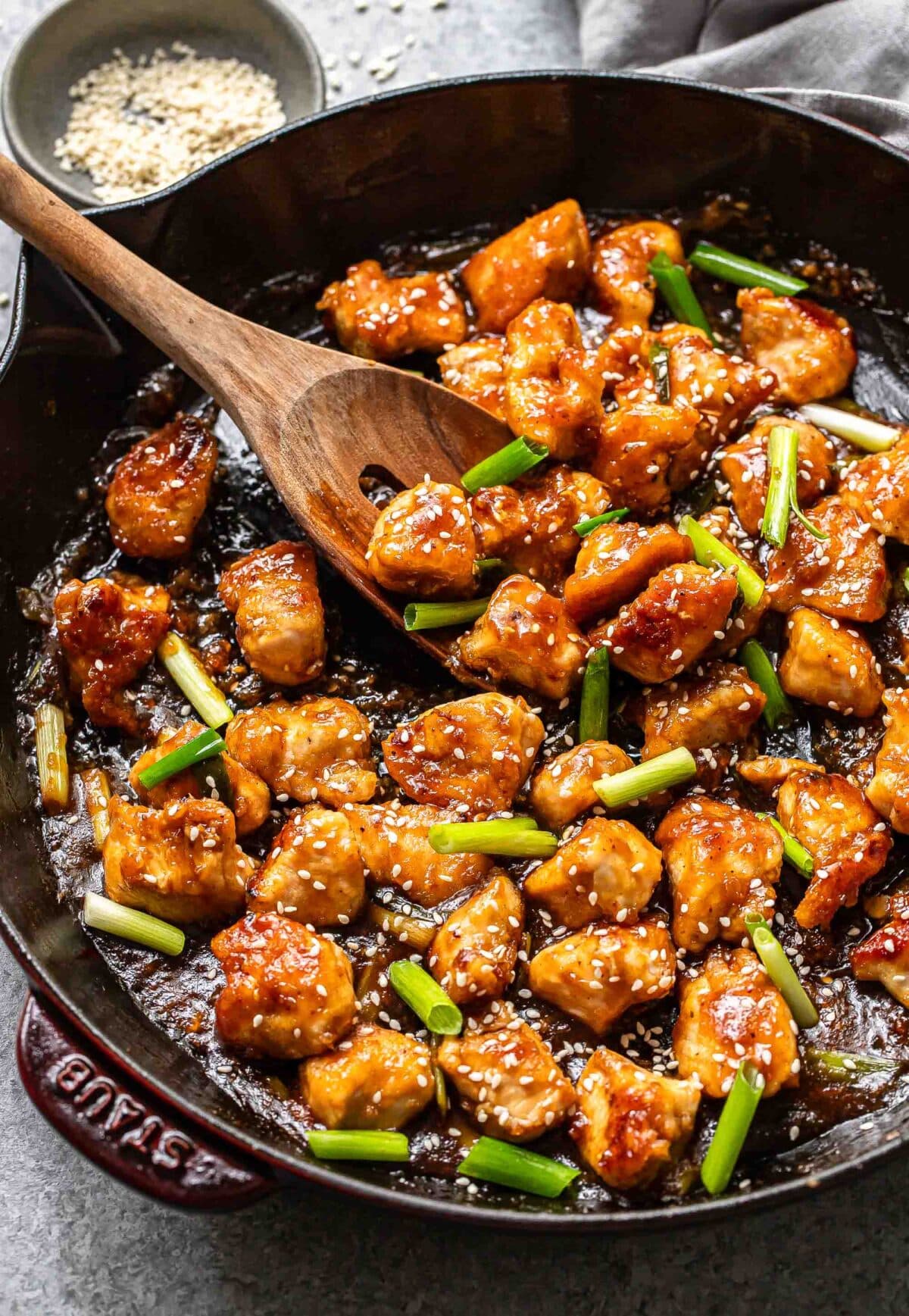 Mongolian chicken in a skillet with a wooden serving spoon.