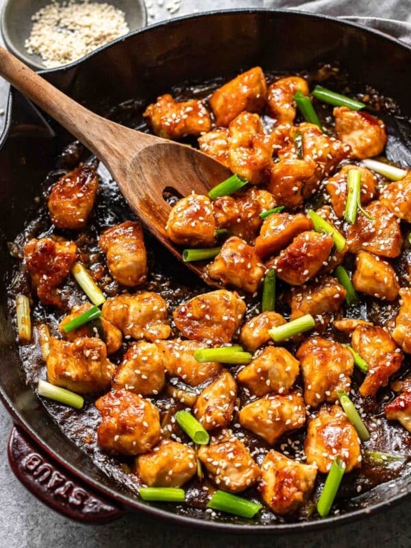Mongolian chicken in a skillet with a wooden serving spoon.