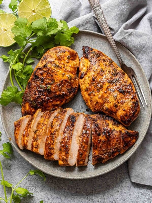 Three southwest grilled chicken breasts on a gray plate with a fork and cilantro. One of the chicken breasts is sliced.