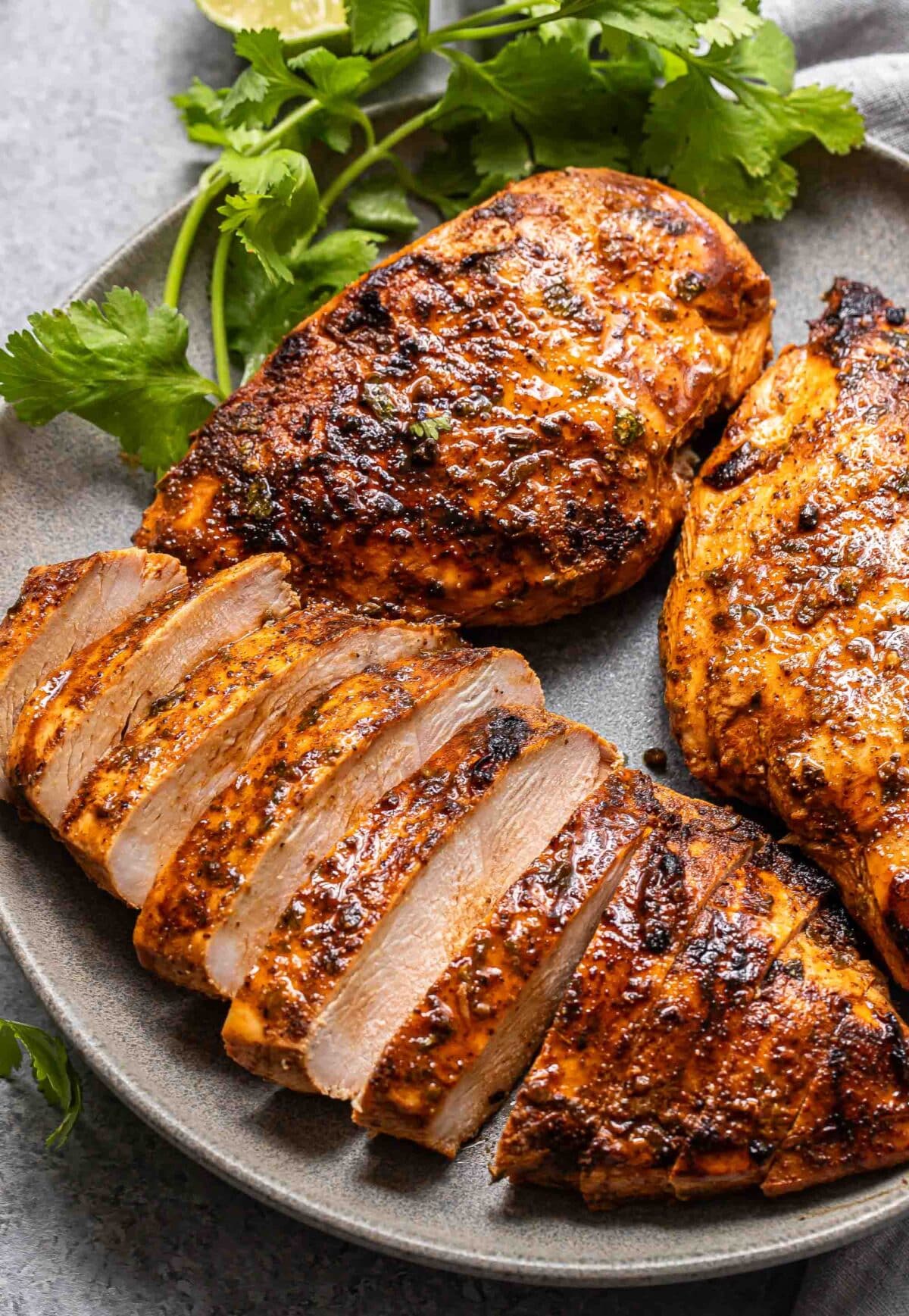 Three southwest grilled chicken breasts on a gray plate. One of the chicken breasts is sliced.