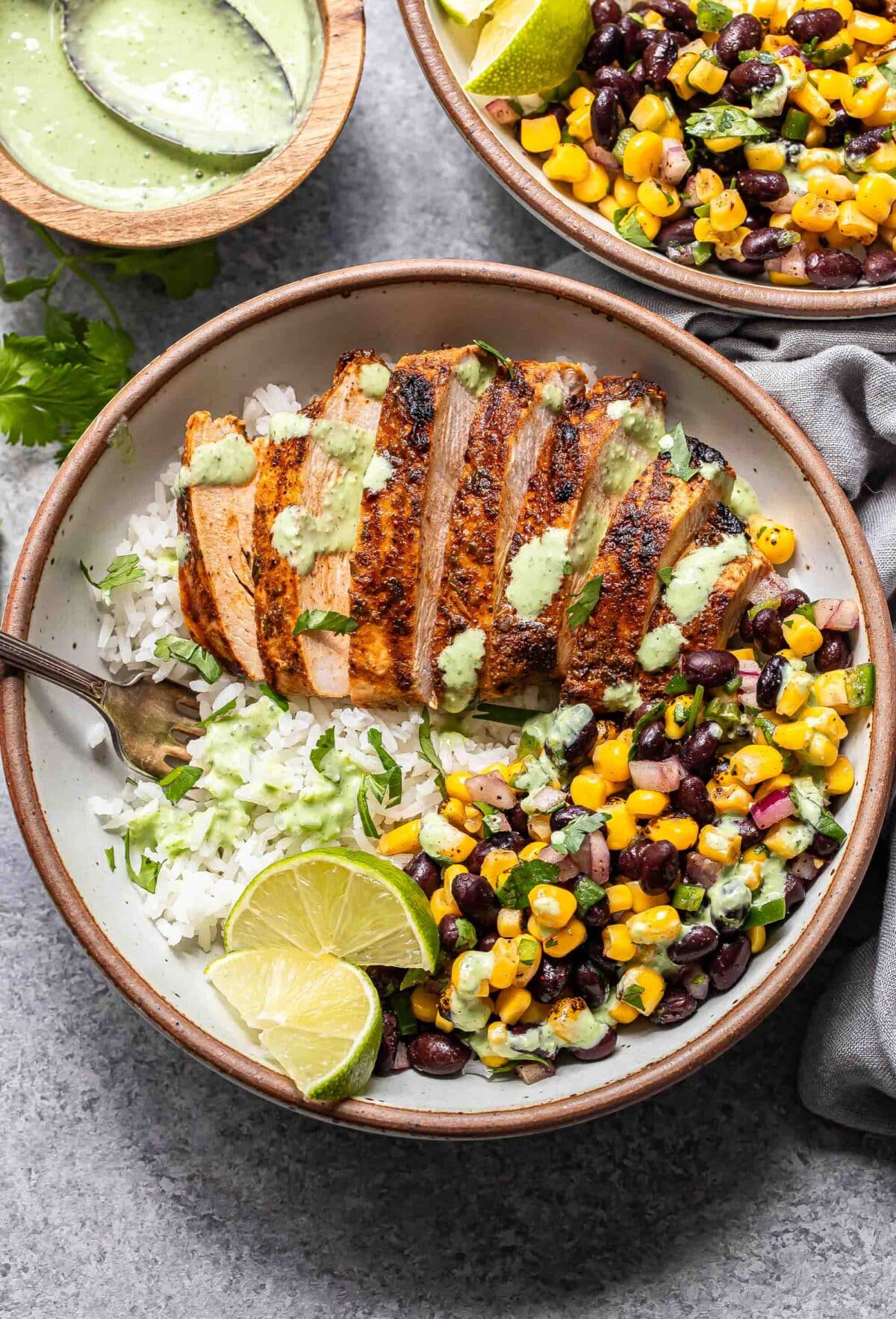 Southwest chicken and rice bowl with black bean corn salsa and cilantro lime dressing in a white bowl with a fork.