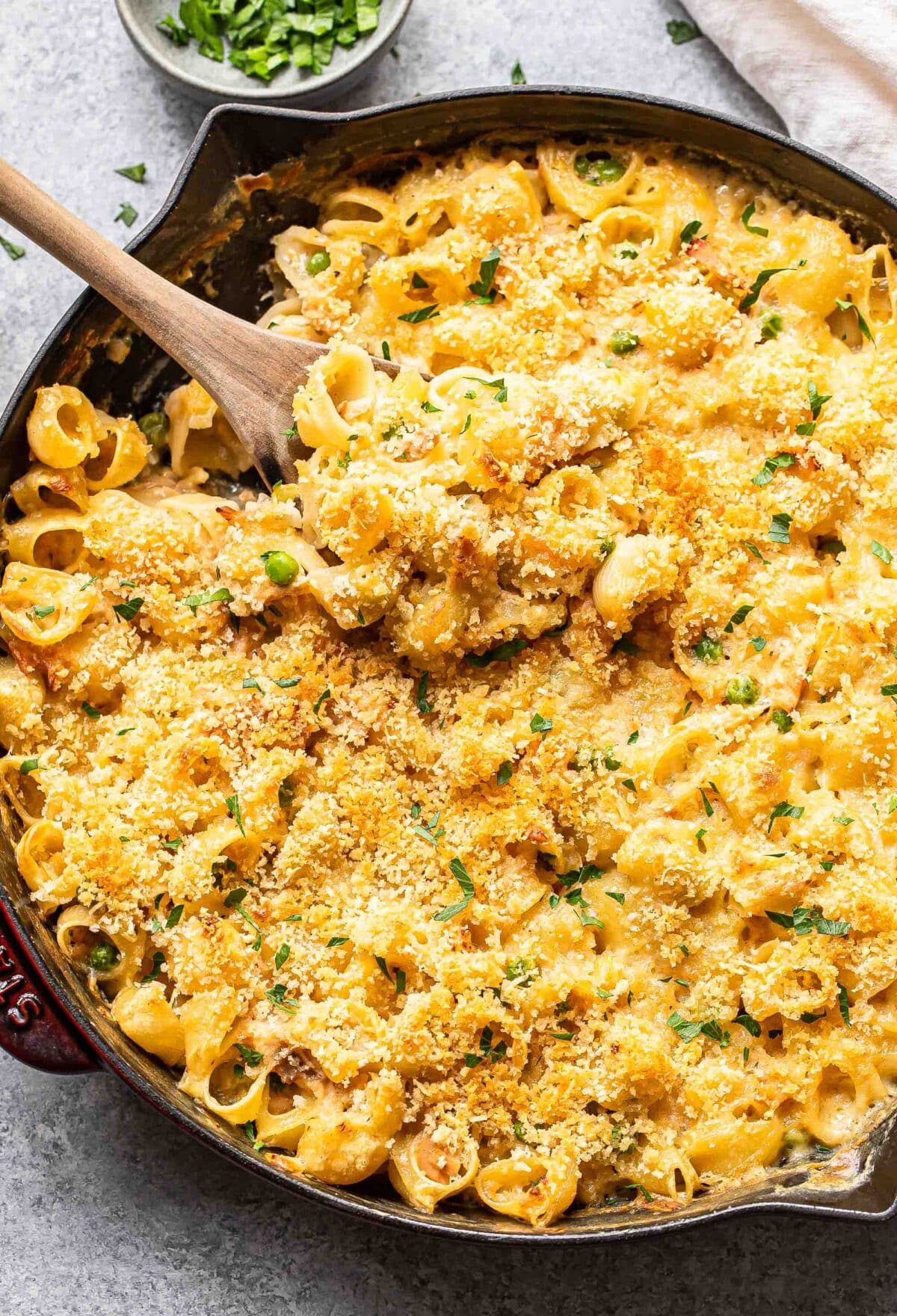 Tuna casserole with panko topping in a skillet with a wooden spoon.