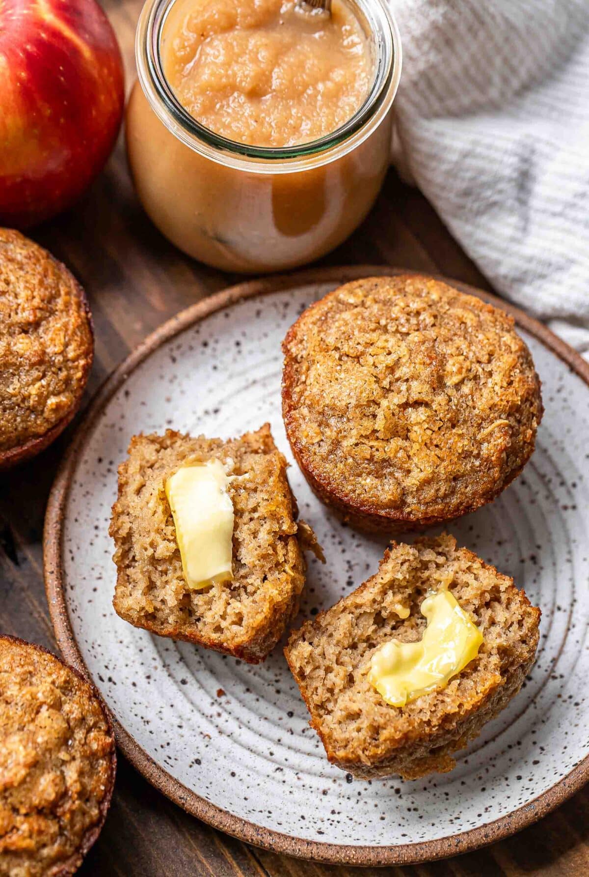 Two applesauce muffins on a plate. One is cut in half and has butter on it.