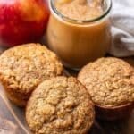 Three applesauce muffins with a jar of applesauce and an apple behind them.