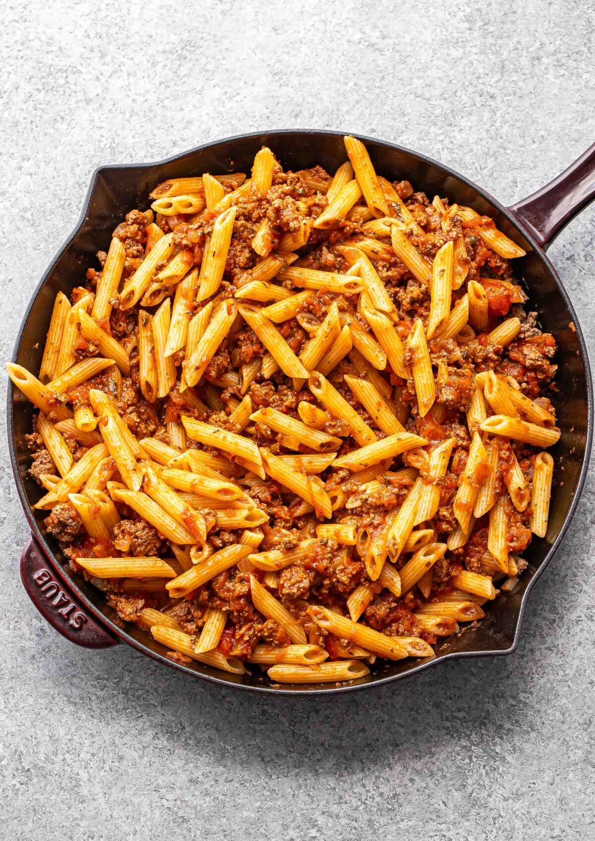 Ground beef, penne, and marinara sauce in a skillet.