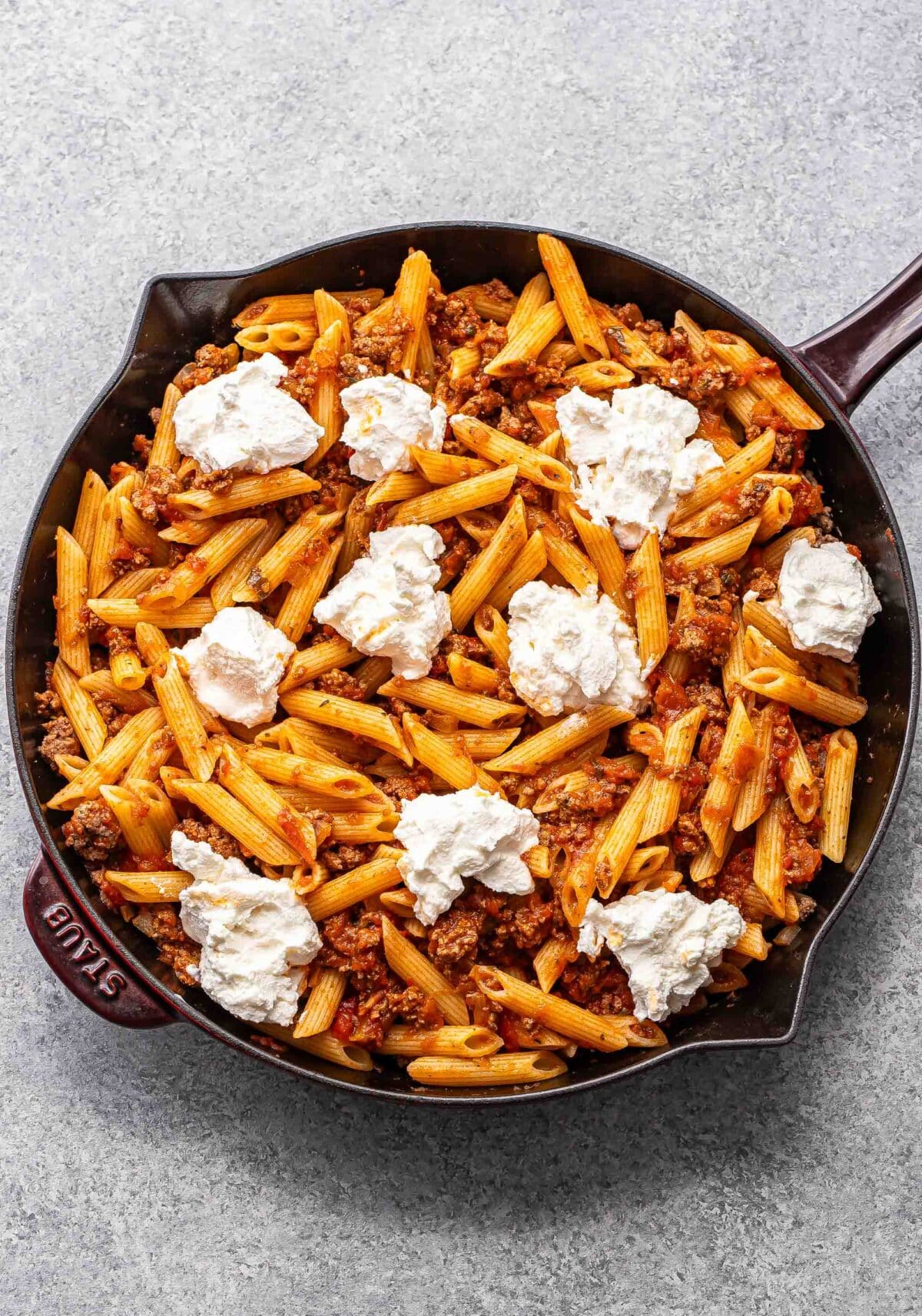Ground beef, penne, and marinara sauce with dollops of ricotta on top in a skillet
