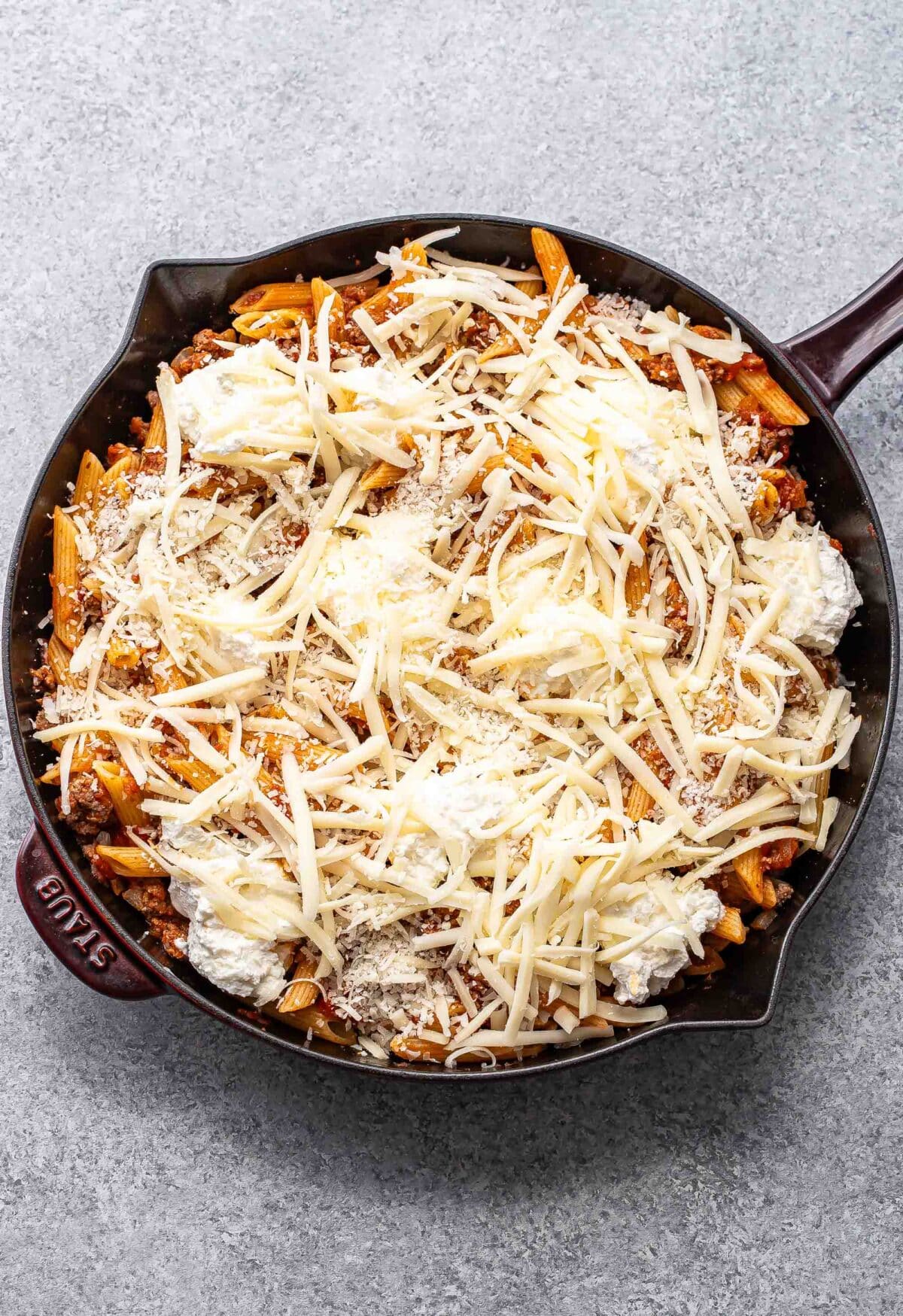 Penne with ground beef and ricotta cheese in a skillet before being baked.