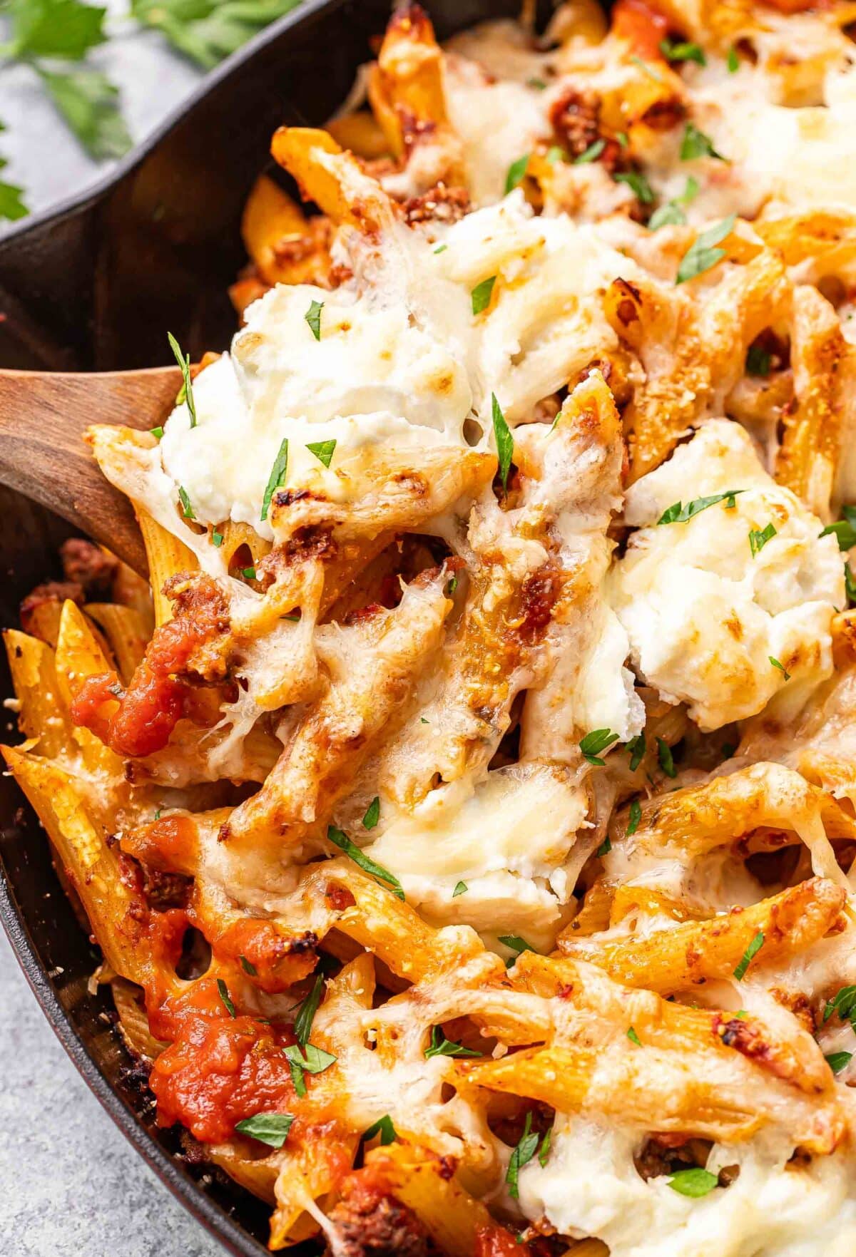 Serving spoon scooping baked penne out of a skillet.