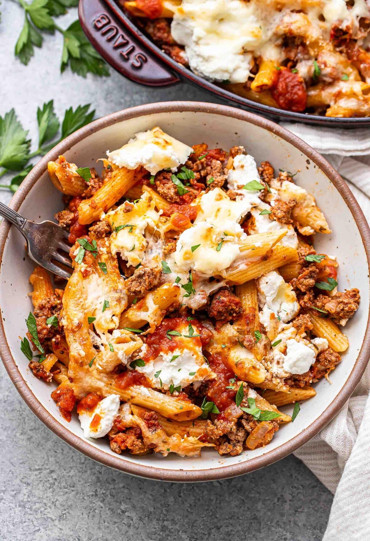 Baked penne with ground beef in a white bowl with a fork.