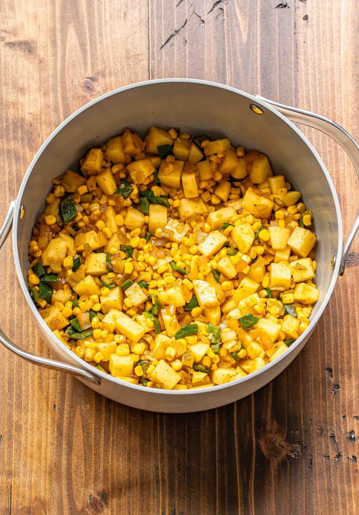 Sauteed pepper, onion, corn, and potatoes in a pot.