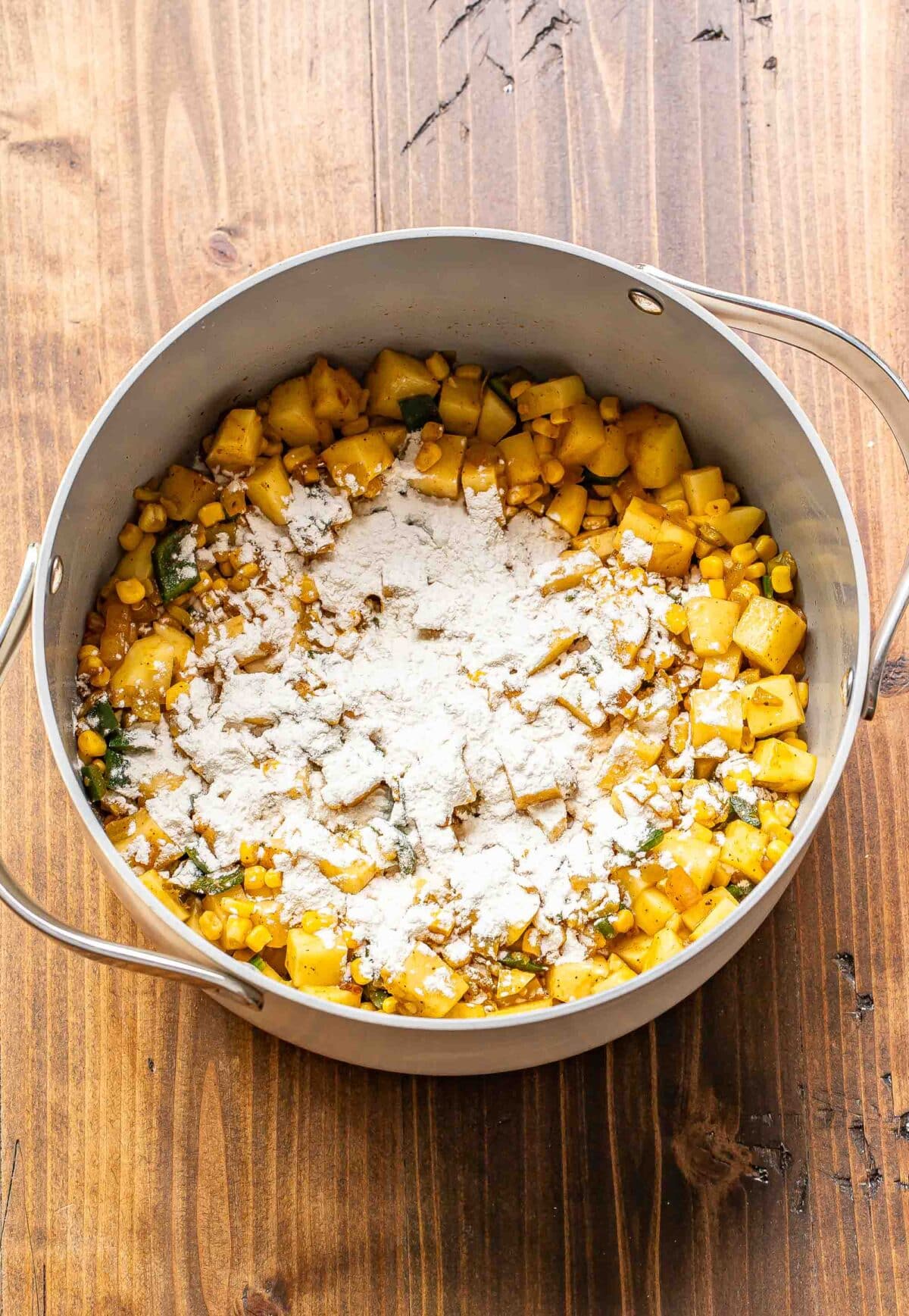 Sauteed pepper, onion, corn, and potatoes with flour sprinkled on top of them in a pot.