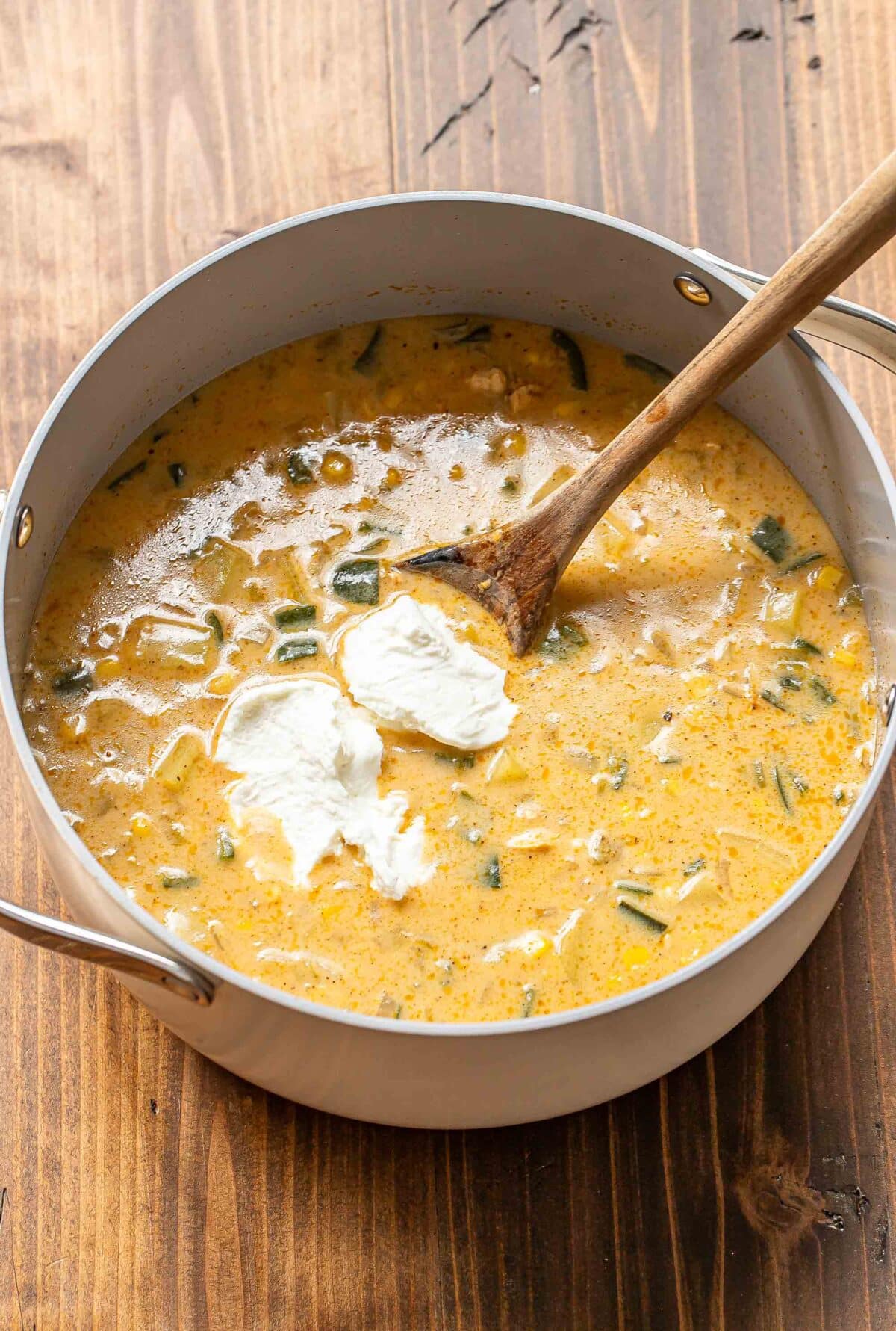 Greek yogurt being stirred into a pot of chicken corn chowder.
