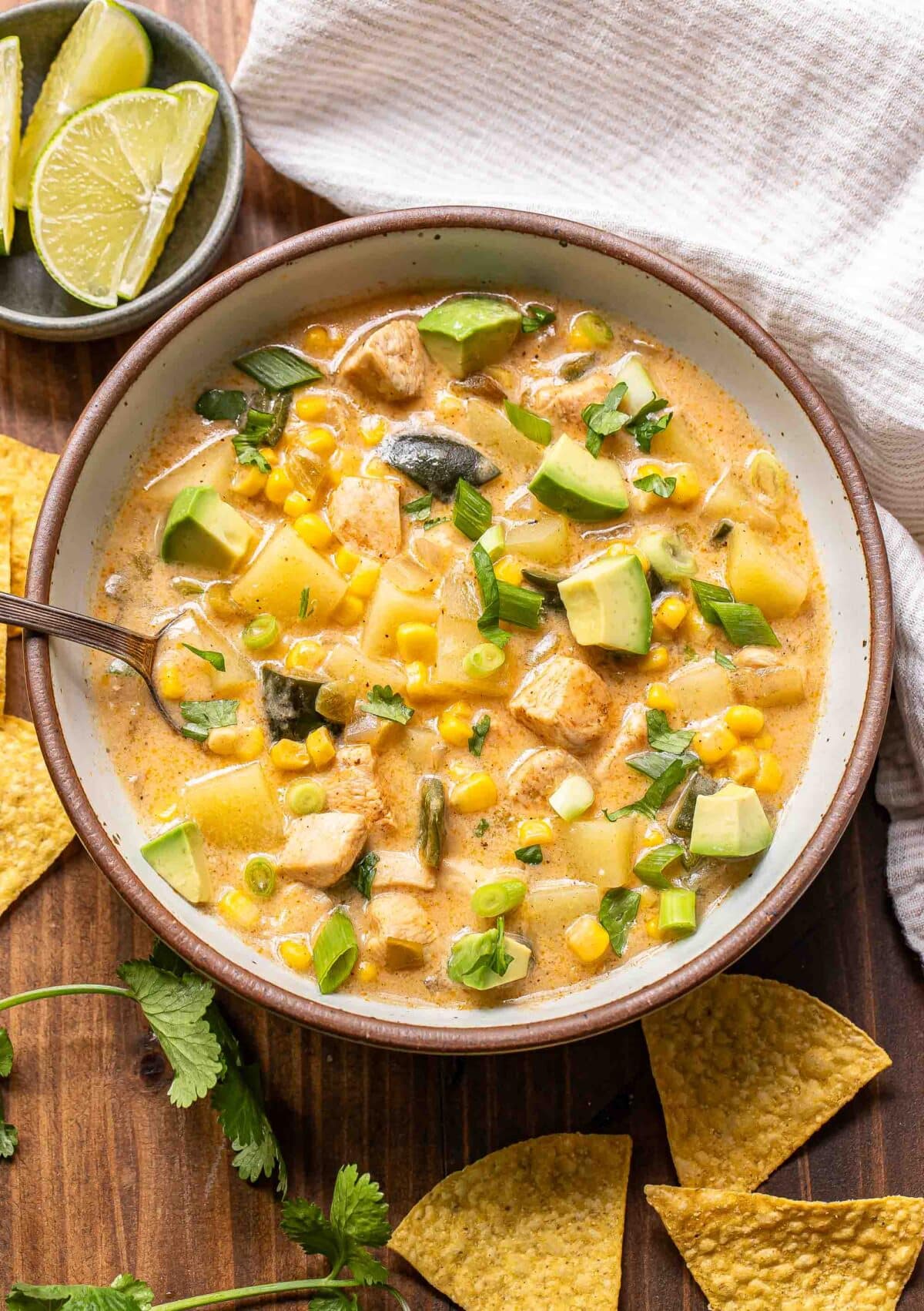 Southwest chicken corn chowder in a white bowl with a spoon and a bowl of limes behind it.