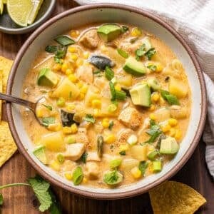Southwest chicken corn chowder in a white bowl with a spoon and a bowl of limes behind it.