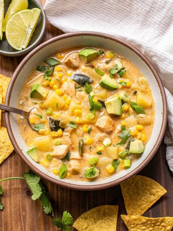 Southwest chicken corn chowder in a white bowl with a spoon and a bowl of limes behind it.