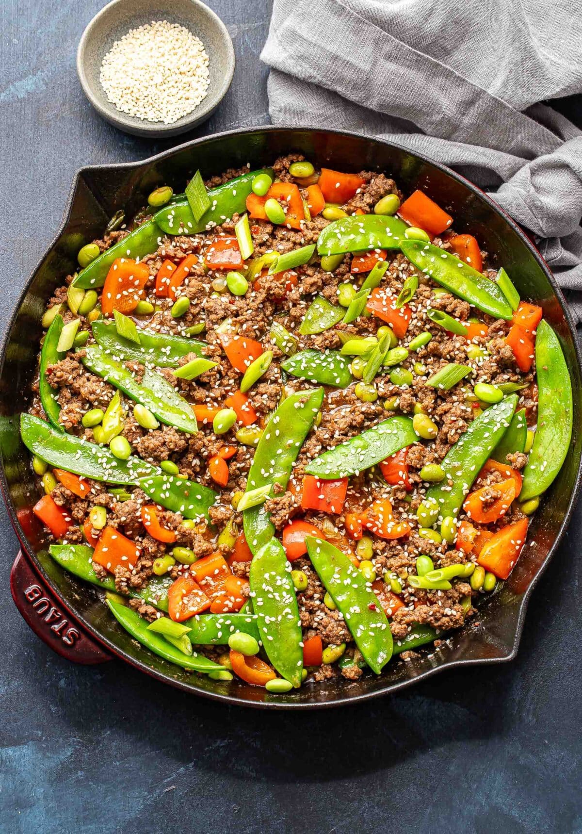 Ground beef stir fry with snow peas, red bell pepper, and edamame in a skillet.