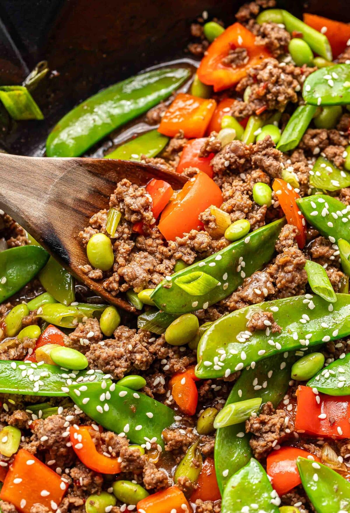 Wooden serving spoon scooping up ground beef stir fry.