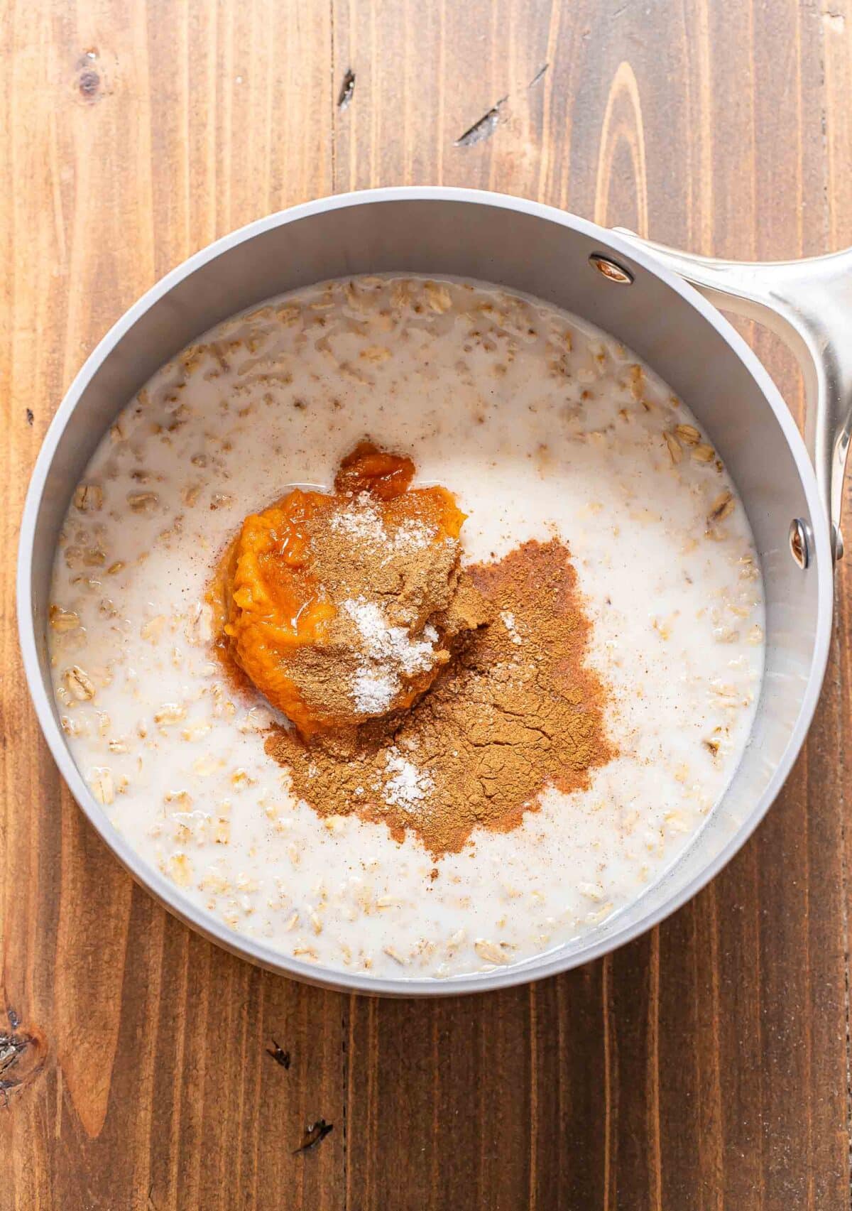 Oats, milk, pumpkin, pumpkin pie spice, and cinnamon in a saucepan.