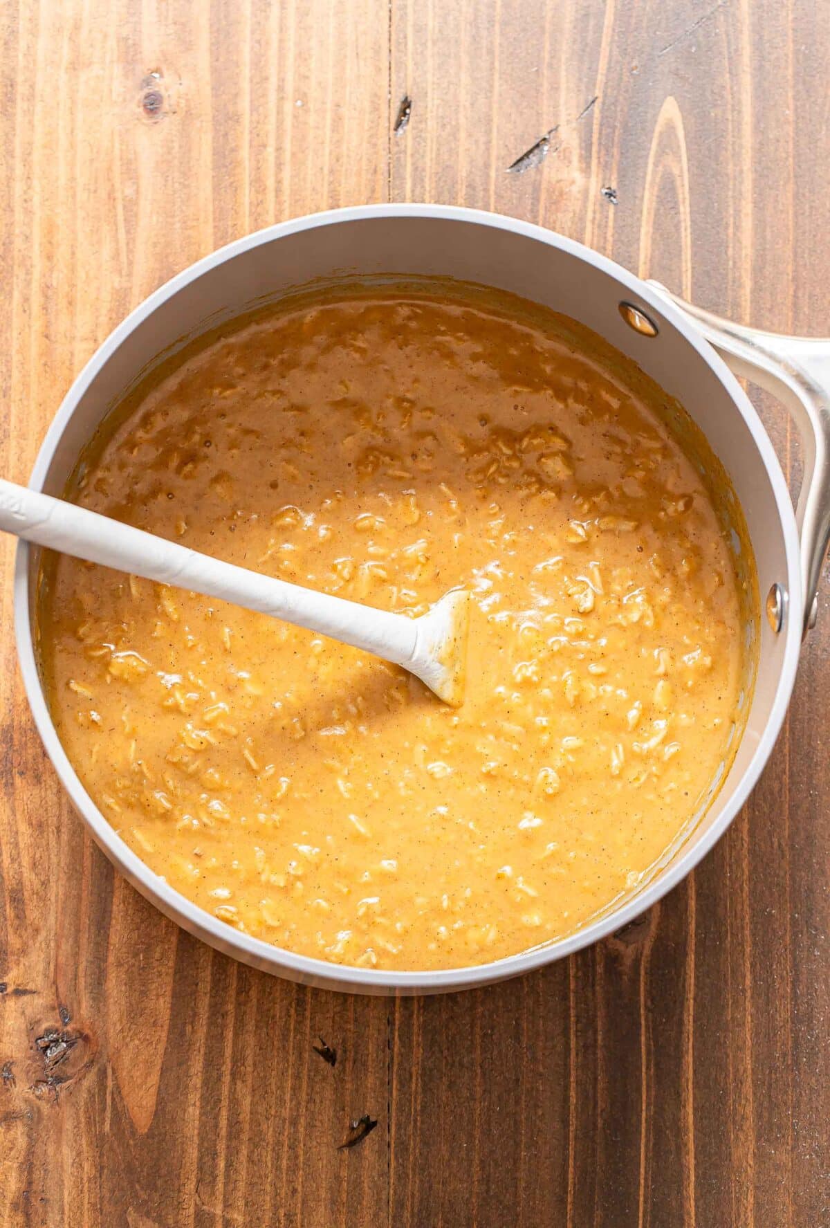 Pumpkin oatmeal in a saucepan with a silicone spatula.