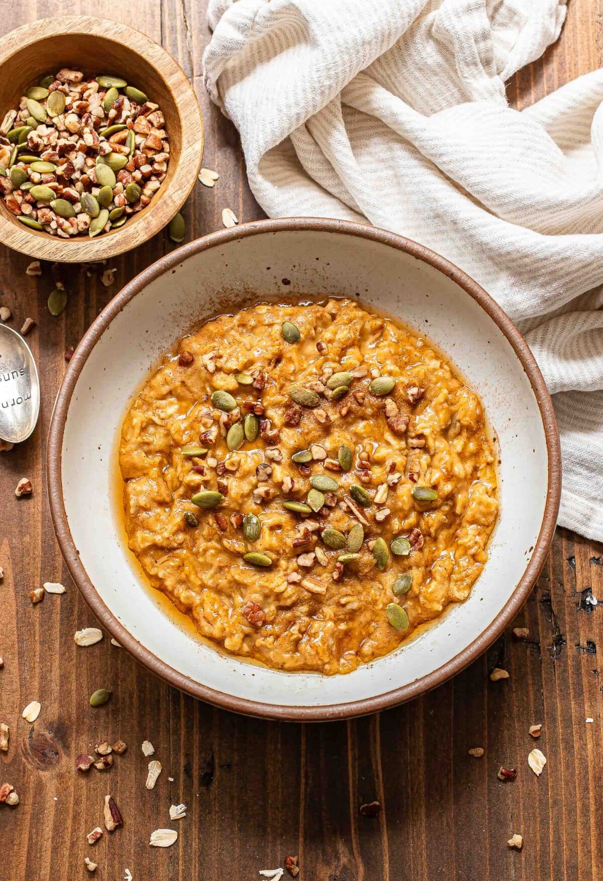 Pumpkin oatmeal in a white bowl topped with pecans and pepitas.