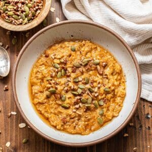 Pumpkin oatmeal in a white bowl topped with pecans and pepitas.