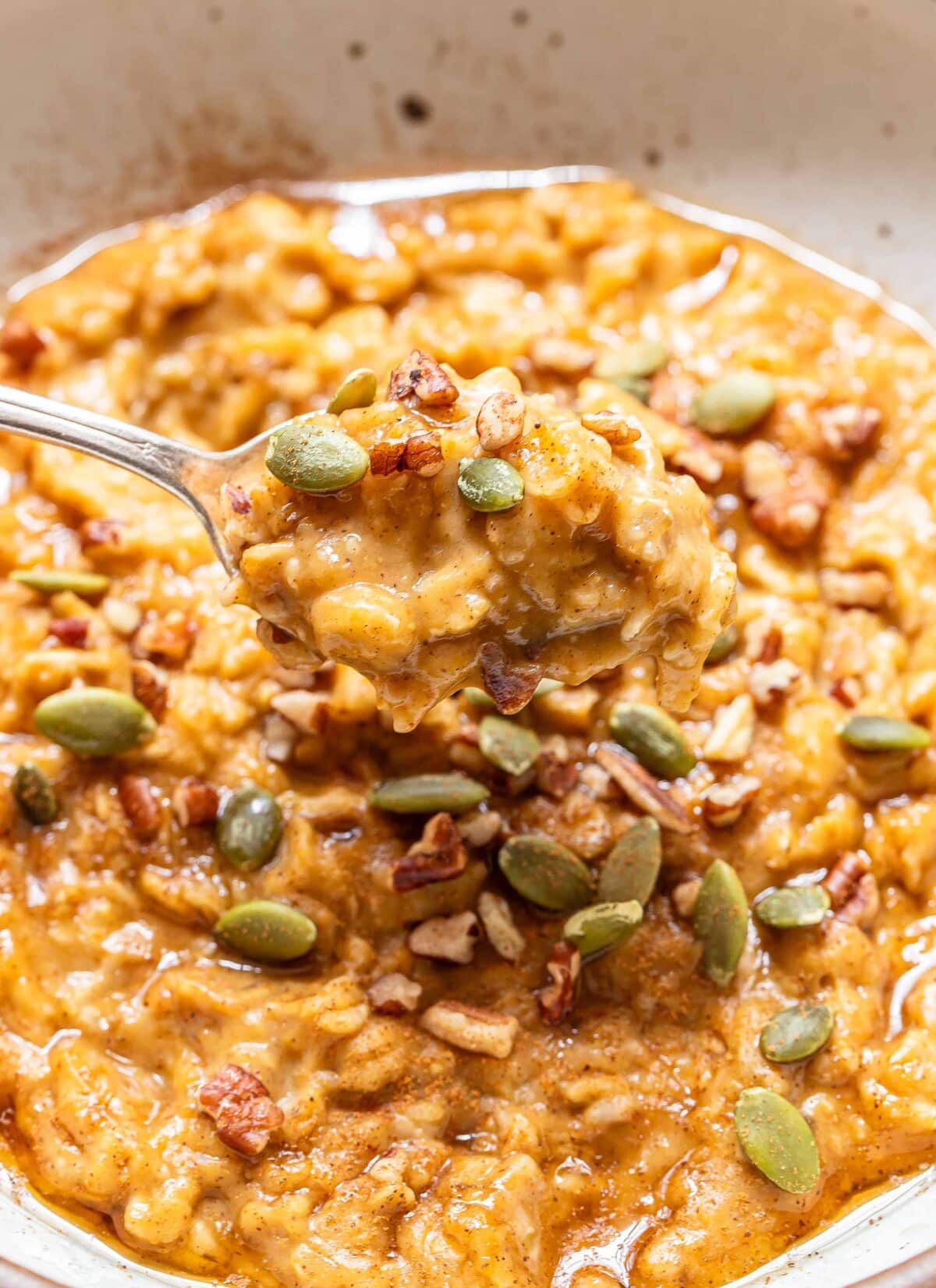 Spoon scooping up pumpkin oatmeal out of a white bowl.