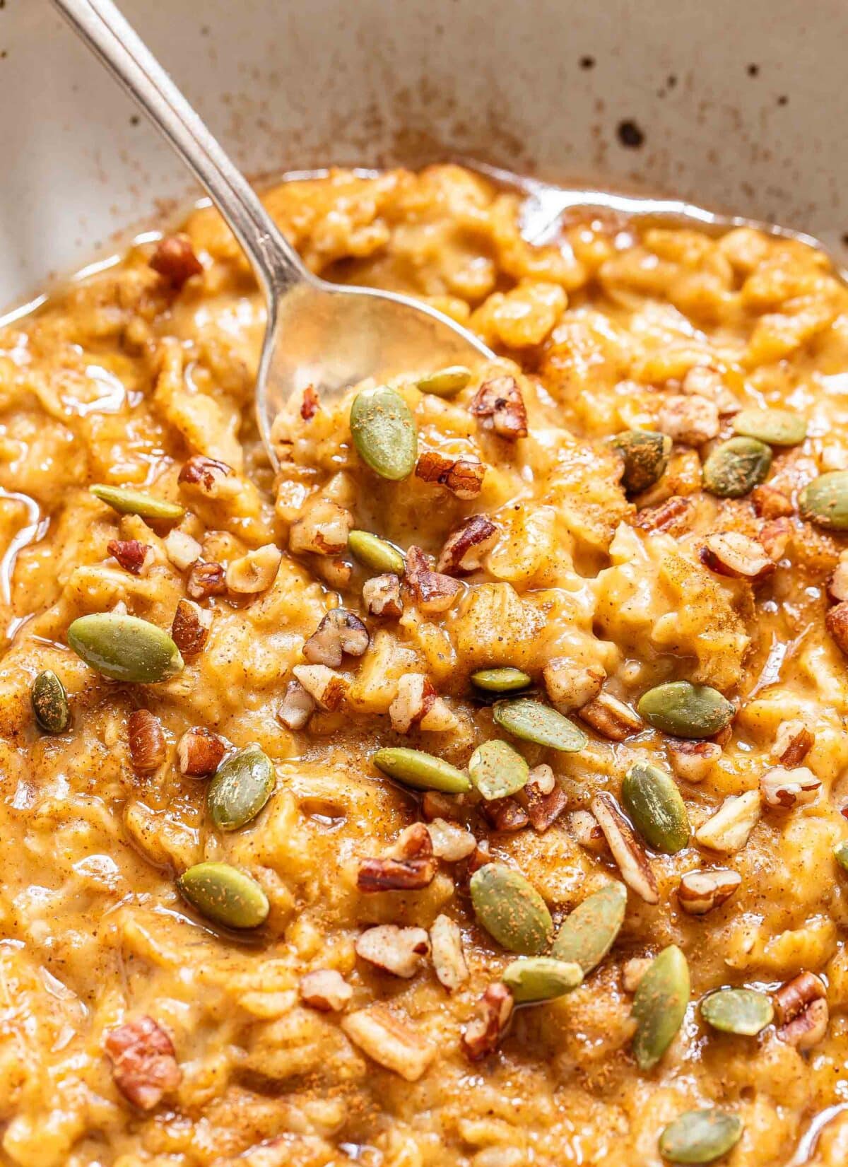 Spoon scooping up pumpkin oatmeal out of a white bowl.