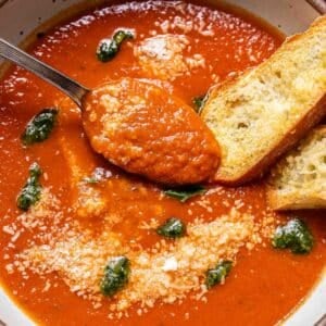 Tomato basil soup with pesto in a white bowl with a spoon and two slices of baguette.