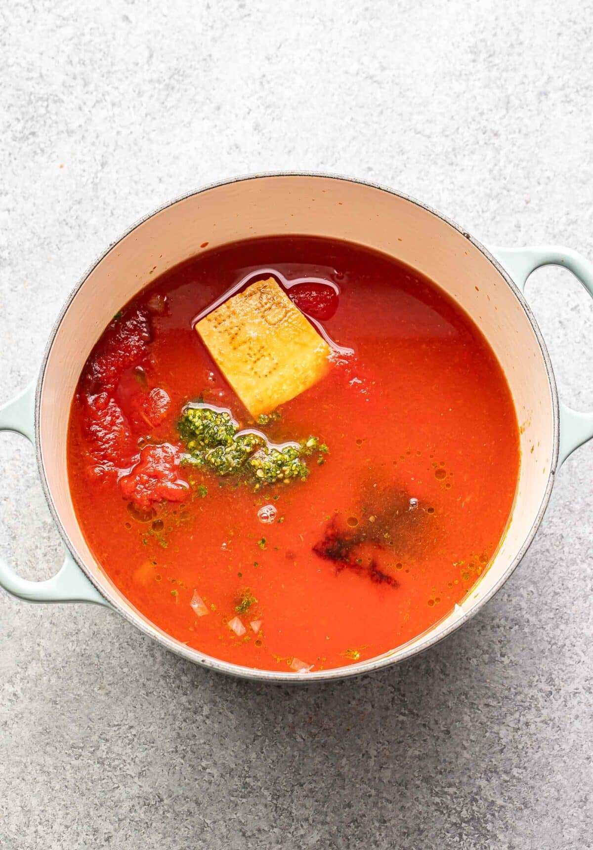 Tomatoes, broth, pesto, and a parmesan cheese rind in a pot.