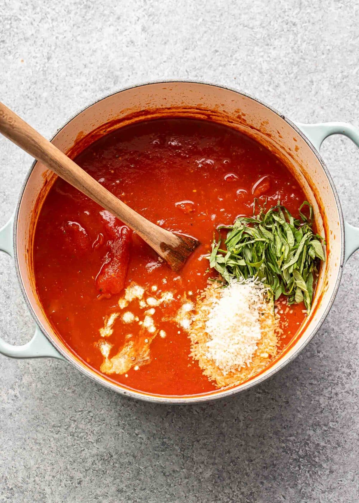 Tomato soup in a pot with parmesan cheese and basil on top that need to be stirred in.