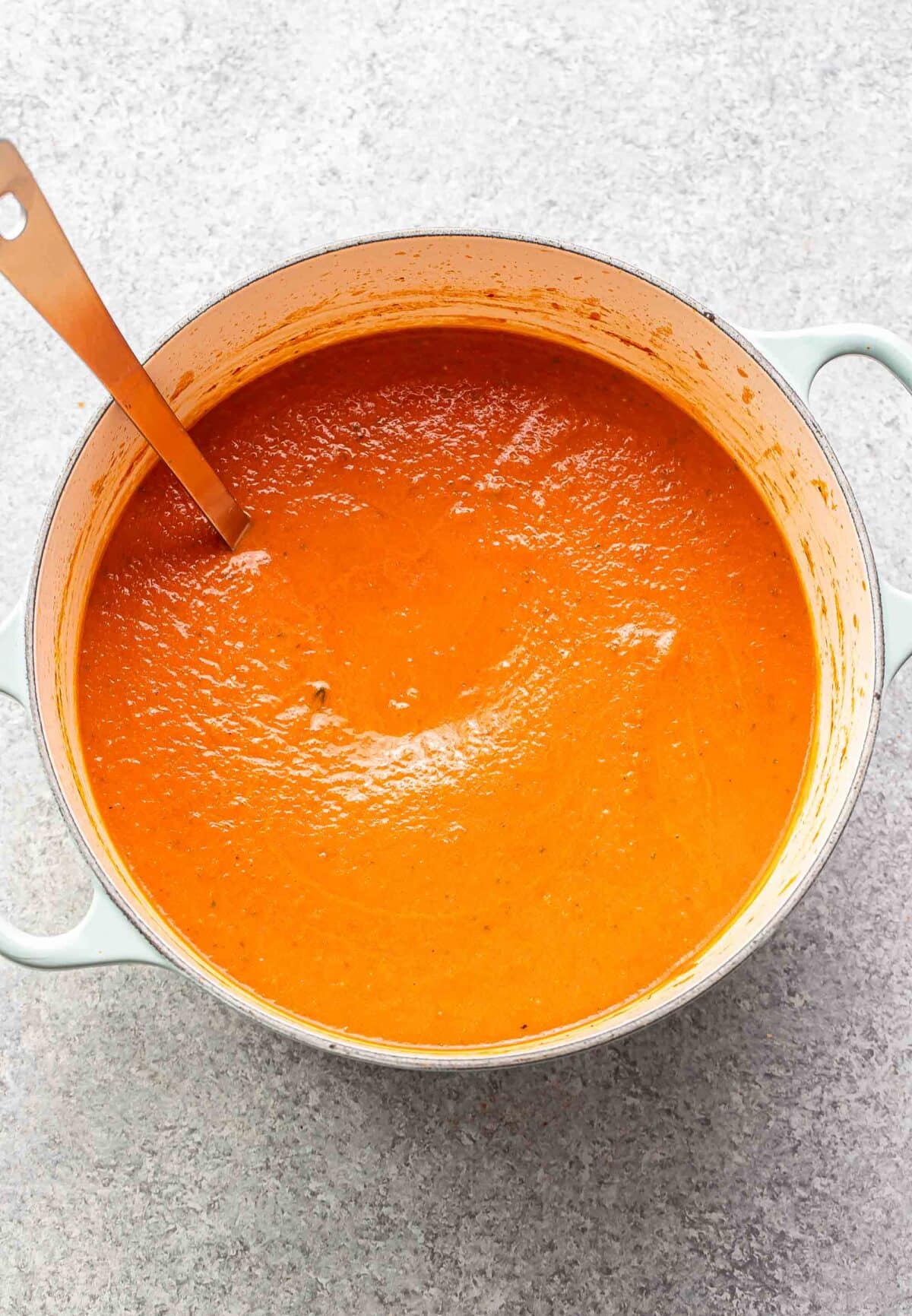 Creamy tomato basil soup in a pot with a ladle.