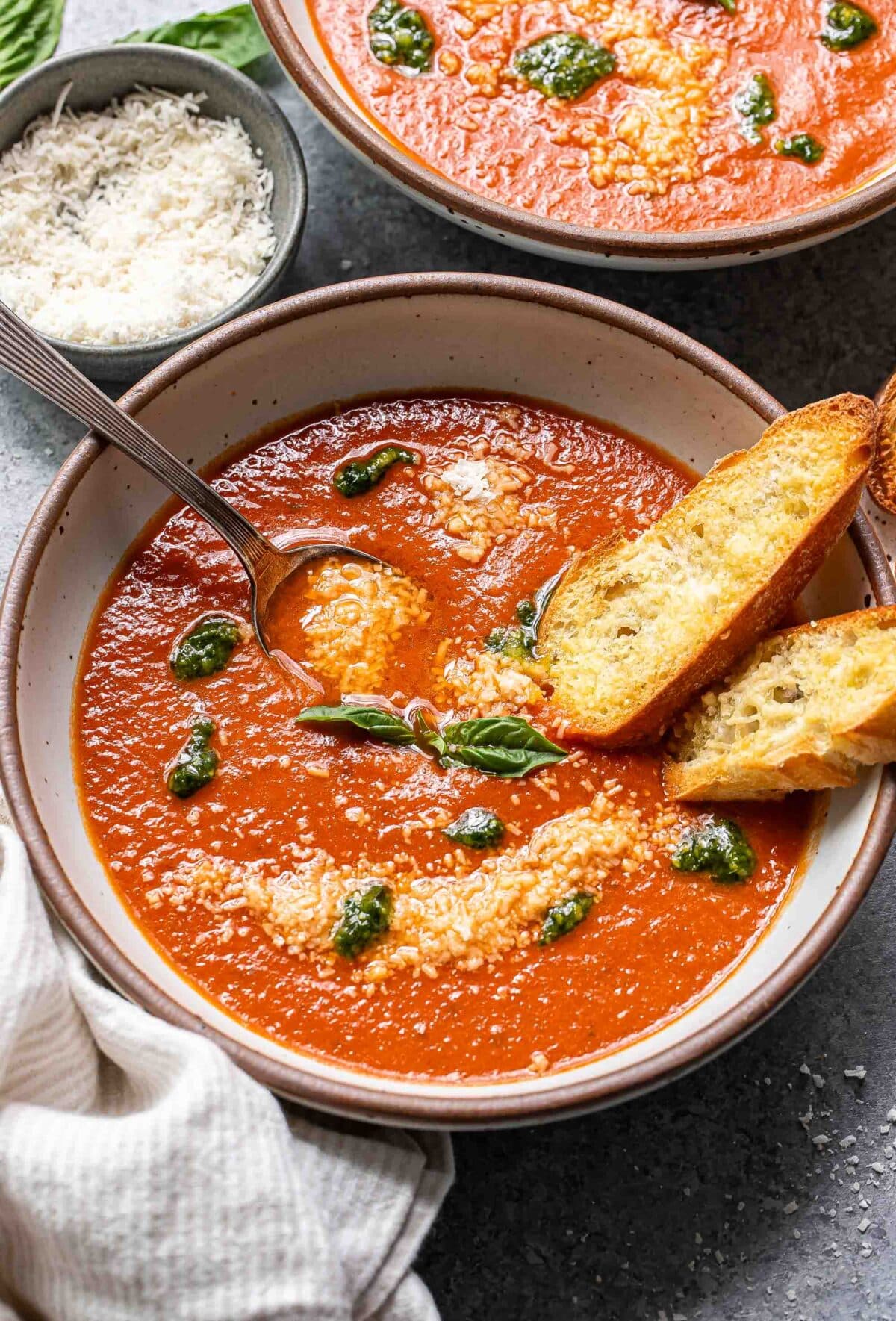 Tomato basil soup with pesto in a white bowl with a spoon and two slices of baguette.