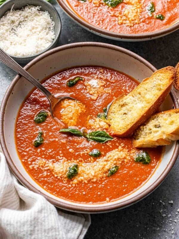 Tomato basil soup with pesto in a white bowl with a spoon and two slices of baguette.
