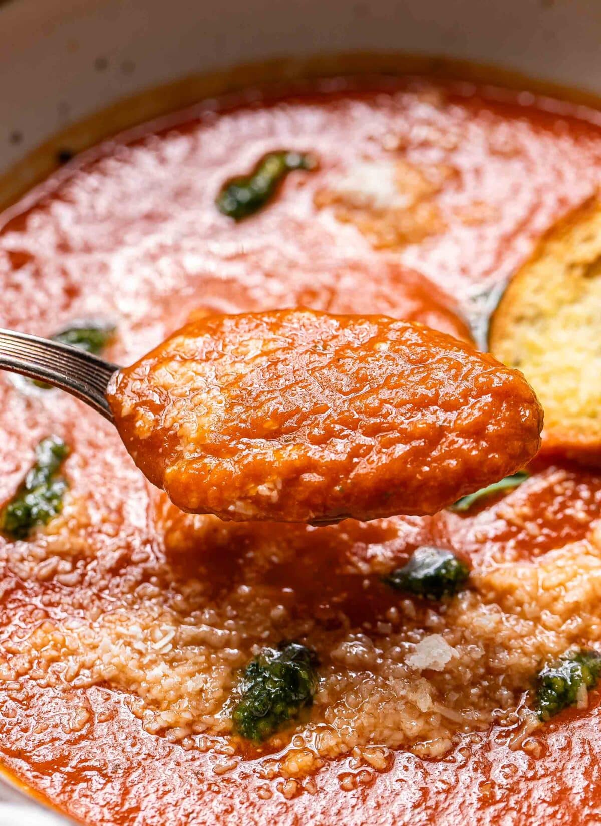 A spoon holding up a spoonful of tomato basil soup.