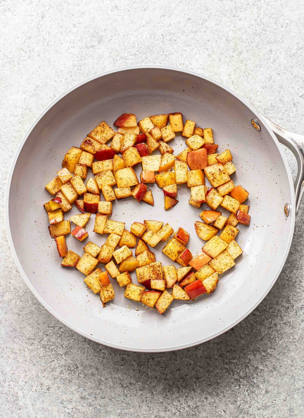 Cooked diced apples with cinnamon in a skillet.