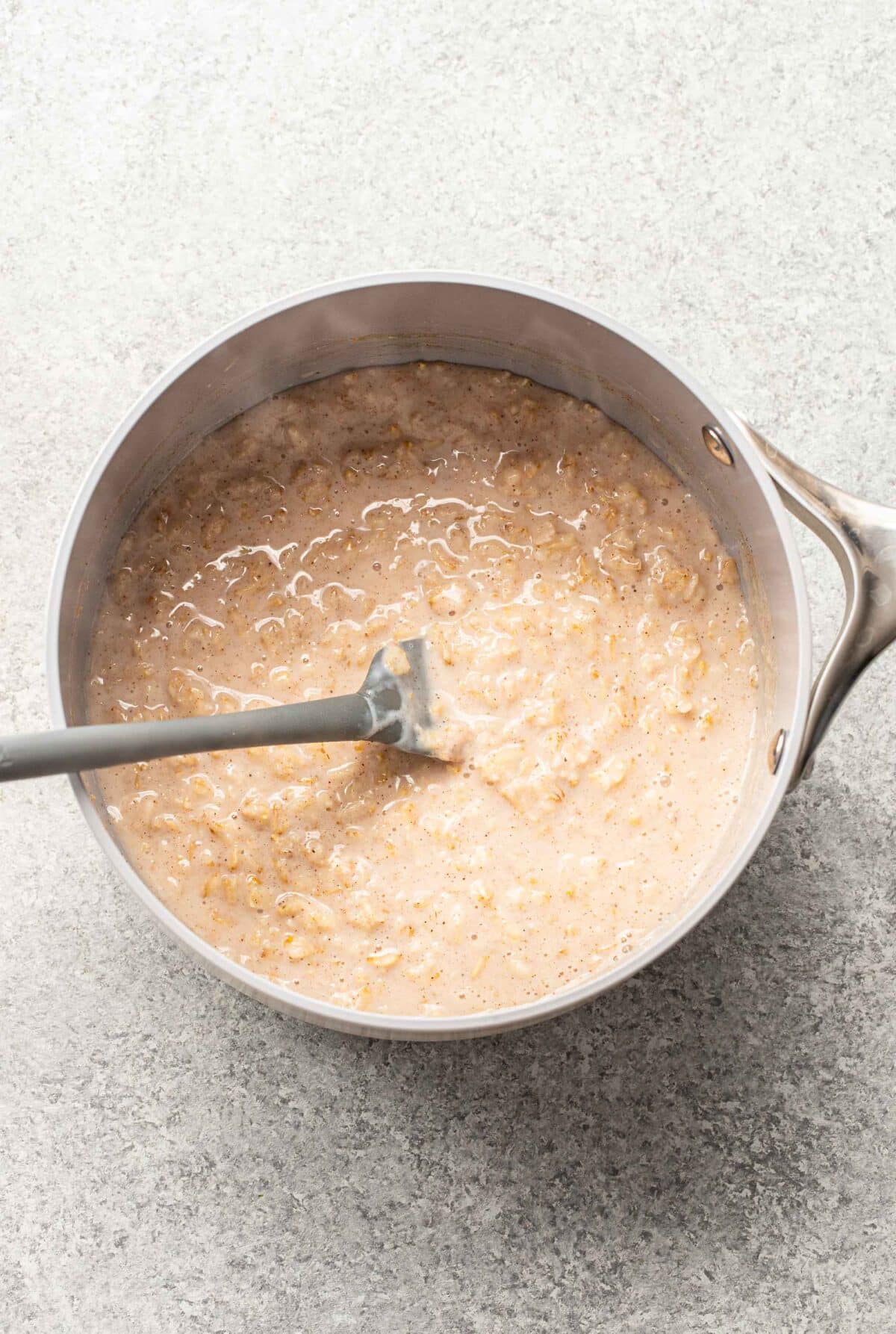 Oatmeal in a saucepan with a rubber spatula.