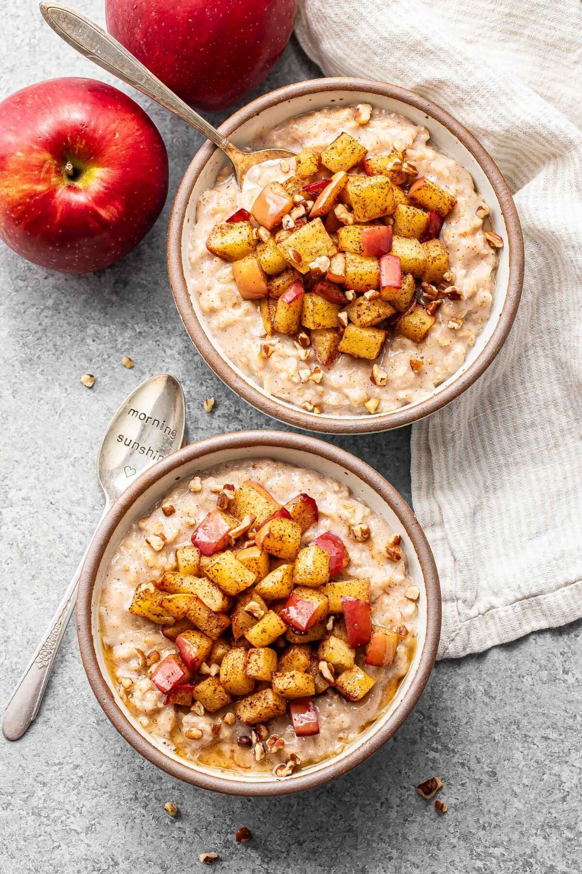 Two bowls of oatmeal with cooked cinnamon apples on top.